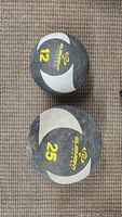 Top view of both Element Fitness medicine balls showing 12lb and 25lb weights on a carpet.