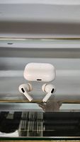Top view of white AirPods Pro charging case and pair of wireless earbuds with silicone tips on a reflective surface.
