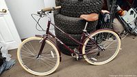 Side view of maroon CCM cruiser bike showing frame, beige tires, saddle and handlebar.