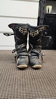 Front view of pair of black Fox dirt bike boots with logos and buckle fasteners