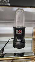 Full view of Magic Bullet single shot blender with clear blending cup attached on base, power cord visible.