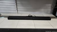 Full length view of the black Sony sound bar speaker on white tiled floor.