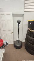 Full view of black freestanding adjustable speed bag in room near door and stacked tires.
