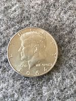 Obverse side of a 1964 Kennedy half dollar coin featuring JFK profile and date.