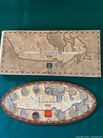 Full view of the rectangular box with map design and the oval display case containing 15 Canadian coins dated 1999.