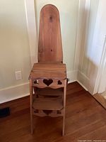 Front view of the wooden 3-in-1 multifunctional piece with ironing board backrest, chair seat, and stepstool steps showing heart cutouts.