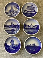 Top view showing the 6 decorative plates arranged in two rows, each plate featuring distinct blue and white scenic designs including ships, buildings, and a church.