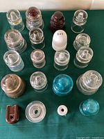 Top-down view of collection of 19 electrical insulators with various shapes and materials on green cloth.