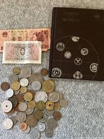 Photo showing the assortment of foreign coins, two banknotes, and the coin album on a gray fabric surface.