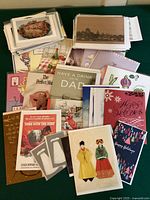 Photo showing a pile of greeting cards including various designs such as holiday themes, floral, and illustrated characters.