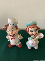 Both vintage Salty and Peppy shakers shown together on beige surface