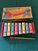 8-key pastel colored tin and wood xylophone in original box, with striking stick in front.