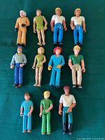 Full display of 12 Fisher Price Adventure People figures showing variety of characters and colors on green cloth.