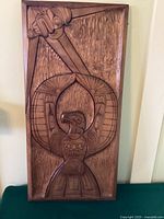 Full view of rectangular carved wood panel leaning against wall