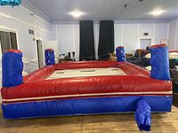 Overall view of square inflatable boxing ring with red and blue sides and corner posts