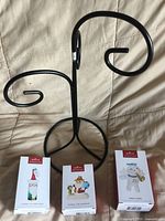 Front view of black metal tree stand with three boxed Hallmark ornaments