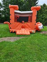 Front view of orange tiger inflatable bounce house showing entrance ramp, mesh window, tiger tail and head detail