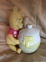 Full view of ceramic honey jar hugged by Winnie the Pooh with lid and dipper