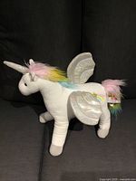 Left side view of white unicorn plush showing silver wings, horn, multicolour mane and tail, GUND tag attached