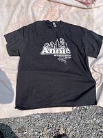 Front view of black Annie graphic T-shirt laid flat outdoors