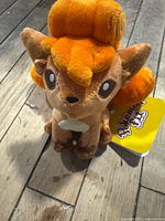 Front view of Vulpix Pokémon Fit plush showing embroidered eyes, nose, curled tail, and tag
