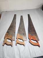 Three vintage hand saws with wooden handles, laid flat to show full shape and blade size.