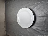 Four large white ceramic plates stacked on top of each other against a grey backdrop.