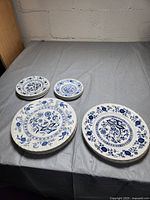 Nine blue and white plates arranged on a grey surface showing distinct floral and Nordic patterns in blue on white ceramic.
