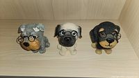 Front view of three dog figurines in gray, beige and black/tan colors, all wearing wire-frame glasses.
