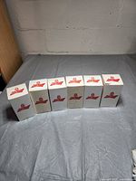 Six Budweiser collectible light-up mugs in their original white boxes with red branding, boxes show dirt marks.