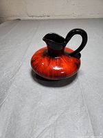 Photo of the decorative water jug showing rounded red and black glazed body with handle and spout.
