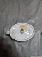 Bottom of one oval white ceramic Denby sauce jug showing black and white Denby mark and sticker label