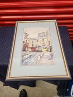 Front view of framed picture depicting outdoor street scene with old buildings.