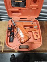 Open orange carrying case with Passlode framing nailer, charger, and plastic components inside.