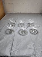 Six clear crystal etched glasses arranged in two rows on grey fabric background, showing pattern and shape from front.