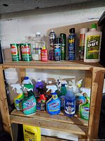 Wooden shelves with multiple cleaning products in different containers including sprays, liquids, and powders