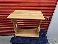 Front-facing image of the wooden side table showing top surface, side supports, and lower shelf.