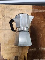 Full view of aluminum stovetop espresso maker with black handle on wooden surface