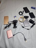 Photo showing an assortment of electronics including power banks, several USB cables, a microSD card with adapter, black wall chargers, and a suction cup mount.