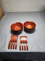 Four stacked wooden bowls and two wooden salad claws laid out flat on a surface.