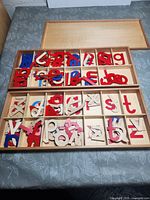 Photo of two wooden boxes containing multiple colorful wooden teaching letters separated by alphabet compartments, lid open