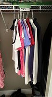 Photo showing 11 women's golf and athletic tops hanging on a rack in various colors and styles, size small