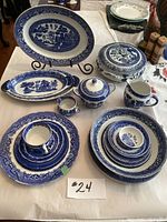 Full display of the 19-piece assorted blue and white Willow china including platters, tureen, plates, cup and jug on a table with stand for platters