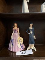 Both vintage Goebel figurines displayed on a dark wood shelf, showing full front view of each figurine