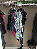 Photo showing eight women's clothing items hanging on a rod including a green plaid skirt, striped shirt, patterned black pants, and others.