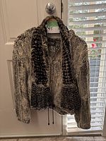 Front view of the Il Fait Froid fur knit coat hanging on a door, showing knit design, hood, and zipper.