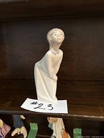 Front view of the glossy white porcelain figurine of a girl in a dress leaning forward.
