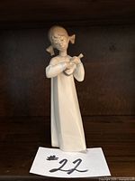 Single close-up of the Lladro Girl with Guitar figurine on a wooden shelf with price tag #22 visible.