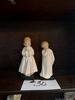 Front view showing both Royal Doulton porcelain figurines named 'Bedtime' and 'Darling' on a shelf with a white paper displaying a lot number.