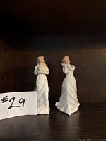 Front view of two Royal Doulton porcelain figurines, ‘Loving You’ and ‘Sweet Dreams’, placed side by side on a shelf with a $29 note nearby.
